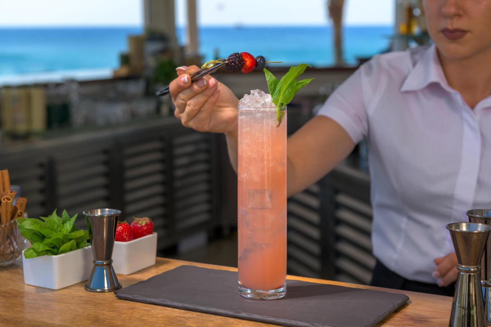 Rodos Palladium Leisure&Wellness Kallithéa Esterno foto A bartender garnishes a cocktail with a fruit skewer.